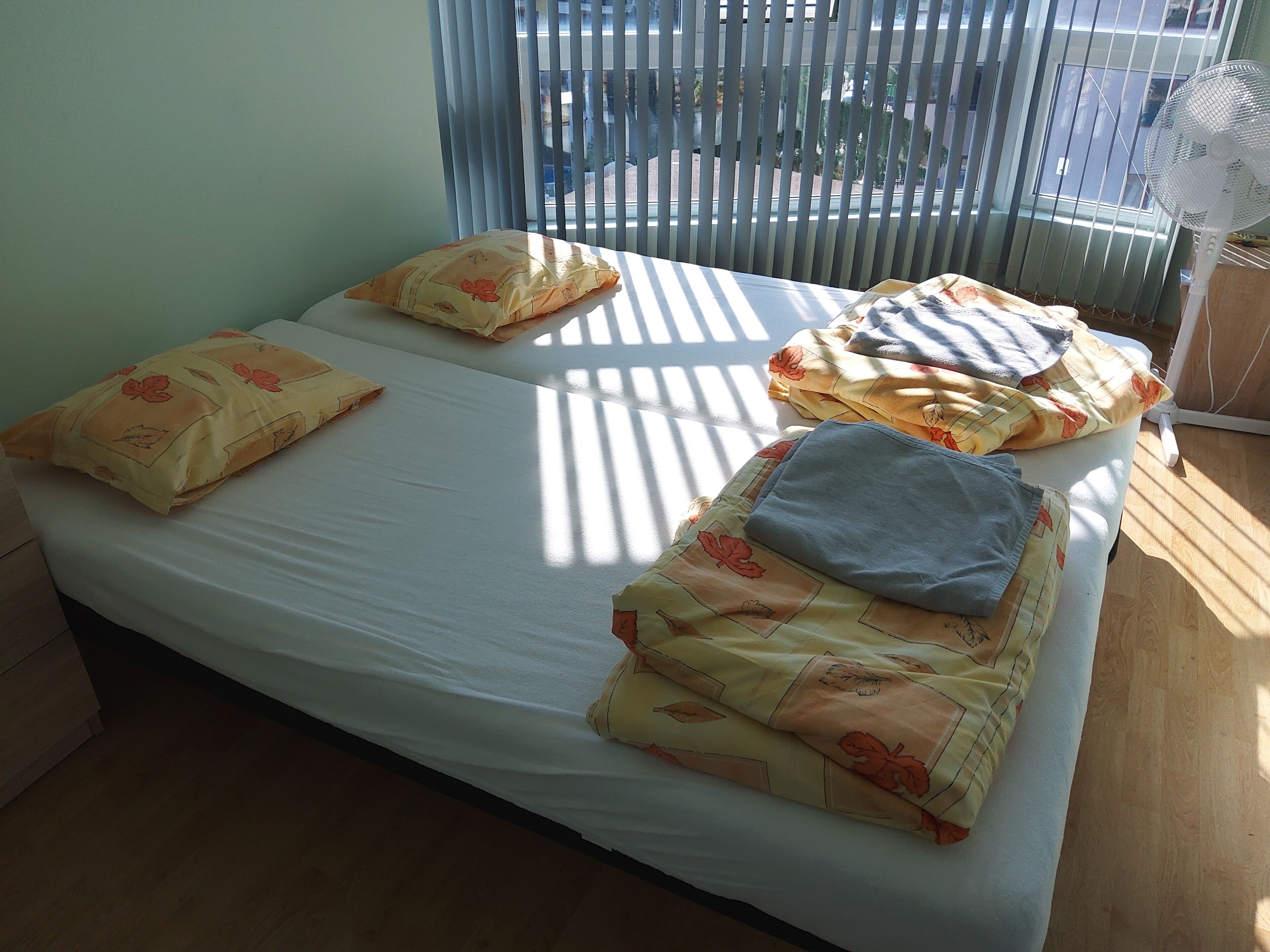 A bed with a white mattress, two pillows with floral patterns, and a blue blanket.