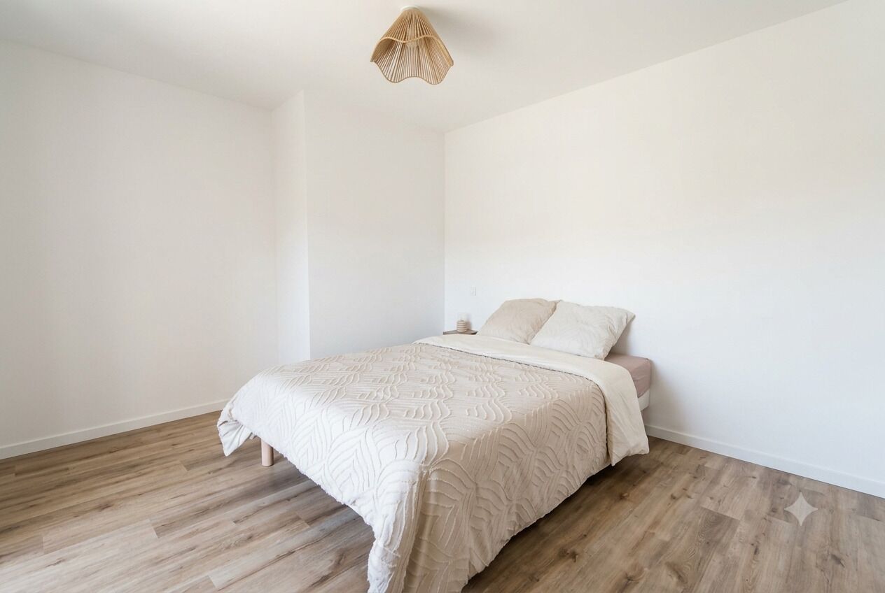 A bedroom with a bed, a bedside table, and a hanging light fixture.
