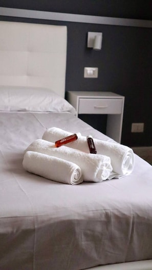 A neatly made bed with rolled white towels and a bottle of lotion.
