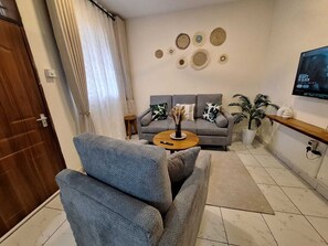 Ein Wohnzimmer mit einer Couch, einem Couchtisch, einem Fernseher, Wanddekoration und einem Blumentopf.