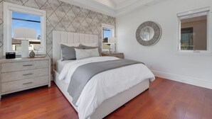A bedroom with a large bed, two bedside tables, a nightstand, a wall clock, and a window. - OCEANFRONT MODERN LUXURY W/ROOFTOP (Newport Beach)