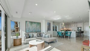 A spacious living area with a large sectional sofa, a round coffee table, and a dining area with teal chairs. - OCEANFRONT MODERN LUXURY W/ROOFTOP (Newport Beach)