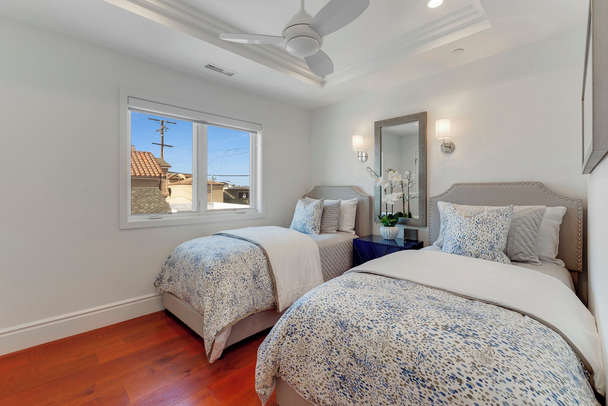 Une chambre avec deux lits, une fenêtre, un ventilateur de plafond et une table de chevet avec une lampe.