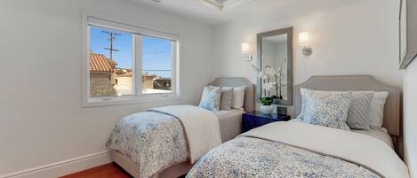 Une chambre avec deux lits, une fenêtre, un ventilateur de plafond et une table de chevet avec une lampe.