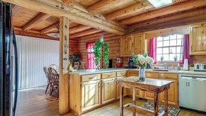 Interior de uma cabana de madeira com cozinha, área de jantar e uma grande janela.