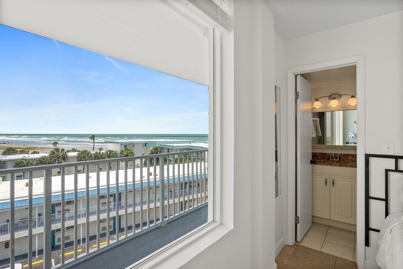 A balcony with a view of the beach and ocean, a small bathroom with a mirror and sink, and a door leading to the interior.