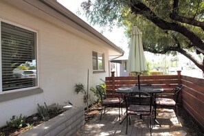 Eine Terrasse mit Tisch und Stühlen, ein Holzzaun und ein Baum, der Schatten spendet.