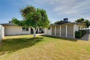 A single-story house with a garage, a lawn, and a tree with yellow flowers. - Casa De Los Caballeros (Scottsdale)