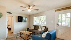 Ein Wohnzimmer mit Deckenventilator, Fernseher, Sofa, Couchtisch und einer Tür mit Fenster.