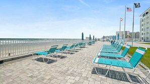 Eine Strandpromenade mit Reihen blauer Liegestühle und Sonnenschirme, einem weißen Zaun und Blick auf das Meer.