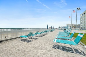 Eine Strandpromenade mit Reihen blauer Liegestühle und Sonnenschirme, einem weißen Zaun und Blick auf das Meer.