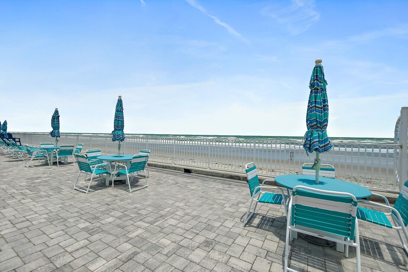 A beachside patio with outdoor seating and umbrellas, overlooking the ocean.