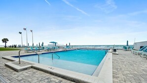 Ein rechteckiger Pool mit einer gefliesten Liegefläche, Liegestühlen und Flaggen.