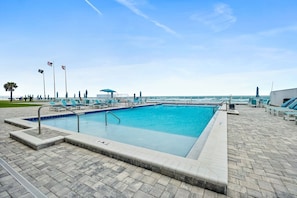 Ein rechteckiger Pool mit einer gefliesten Liegefläche, Liegestühlen und Flaggen.