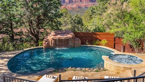 Ein Pool mit Wasserfall, umgeben von einer Holzterrasse und Liegestühlen.