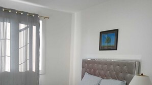 A neatly made bed with a grey headboard, a bedside lamp, and a framed picture on the wall.