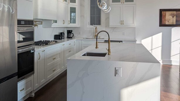 A modern kitchen with white cabinetry, a central island, stainless steel appliances, and a pendant light.