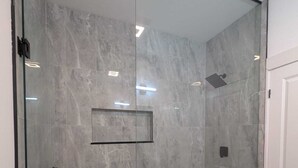 A glass-enclosed shower with a tiled floor and a small shelf.
