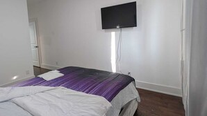 A bedroom with a bed, a flat-screen TV mounted on the wall, and a door in the background.