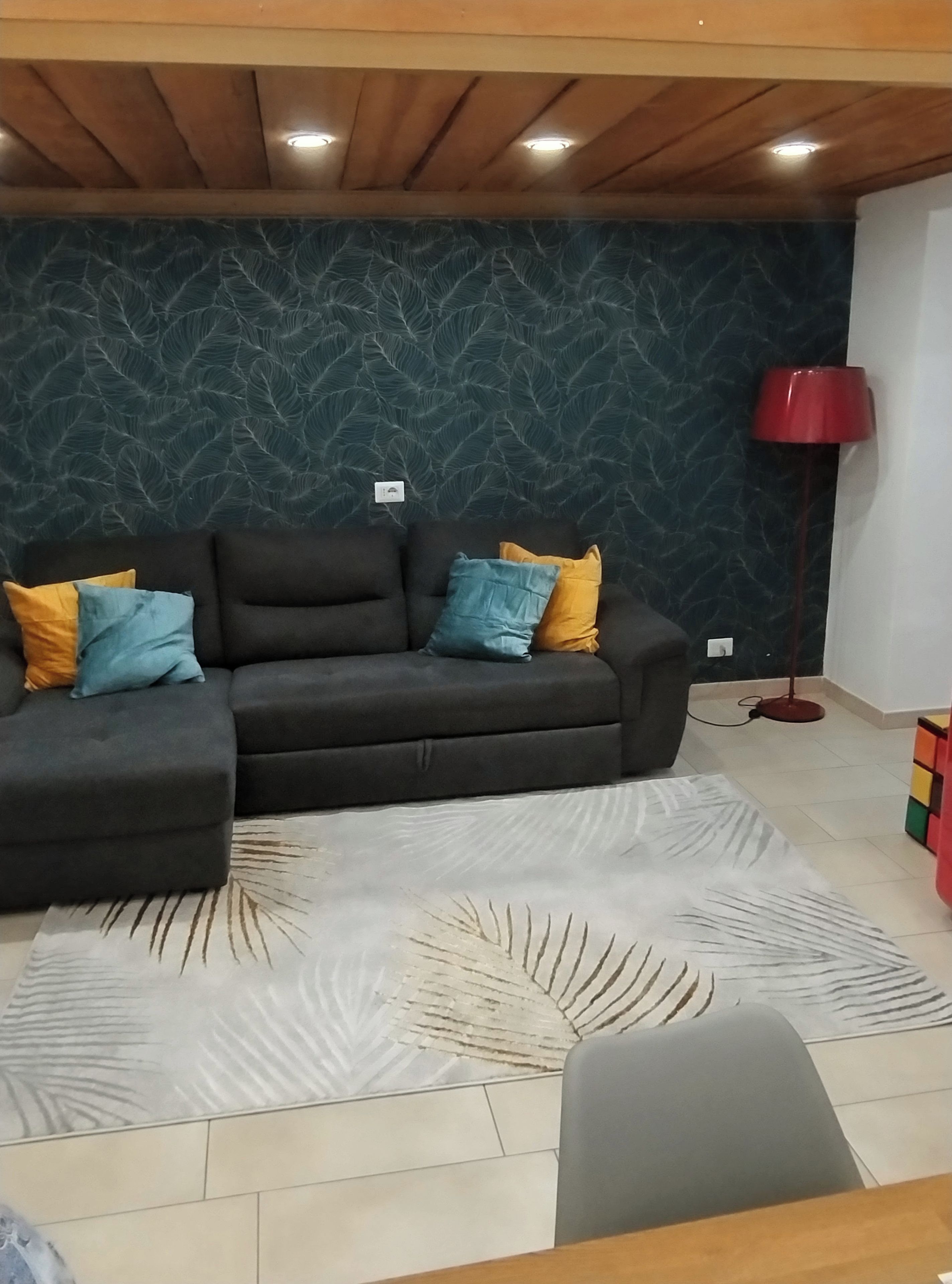 A living room with a dark-colored sofa, a patterned rug, a red floor lamp, and a Rubik's Cube on the floor.