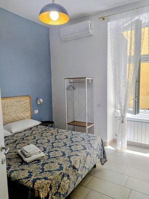 Un dormitorio con cama, perchero, ventana con cortinas y equipo de aire acondicionado.