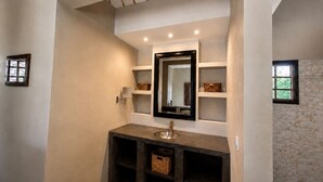 A bathroom with a vanity, mirror, shelves, and a stone wall.