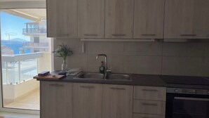 A kitchen with wooden cabinets, a double sink, and a built-in oven. - Upscale Sea-View Apartment in Athenian Riviera (Paleo Faliro)