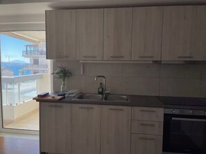A kitchen with wooden cabinets, a double sink, and a built-in oven. - Upscale Sea-View Apartment in Athenian Riviera (Paleo Faliro)