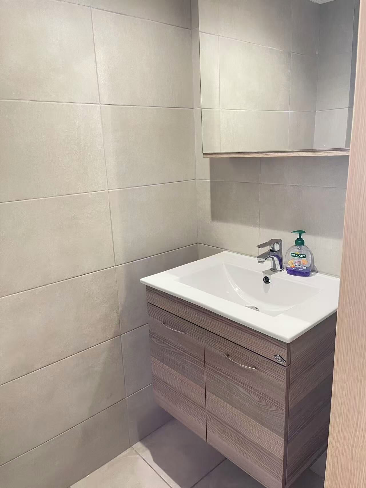Un baño con un lavamanos blanco, un espejo encima y una botella de jabón Palmolive.