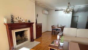 A living room with a fireplace, wooden flooring, a sofa, a dining table with chairs, and a chandelier. - Upscale Sea-View Apartment in Athenian Riviera (Paleo Faliro)