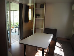 Ein Zimmer mit einem weißen Tisch, einem grauen Sofa, einem Bücherregal und einem Fenster mit Vorhängen.