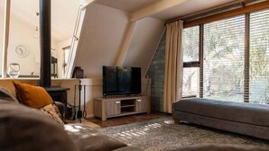 Ein modernes Wohnzimmer mit Fernseher, Sofa und großen Fenstern.