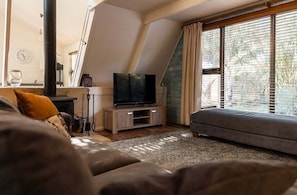 Ein modernes Wohnzimmer mit Fernseher, Sofa und großen Fenstern.