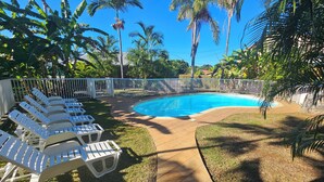 A swimming pool surrounded by white lounge chairs, palm trees, and a white fence. - Ti kaz village Bungalow N°4 (Saint-Louis)