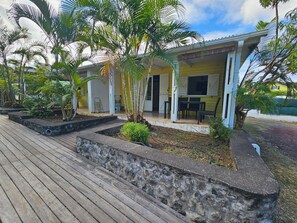 A house with a porch, outdoor seating, and a garden with plants and a wooden deck.