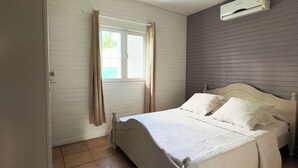 A bedroom with a bed, curtains, an air conditioning unit, and a tiled floor. - Ti kaz village Bungalow N°4 (Saint-Louis)