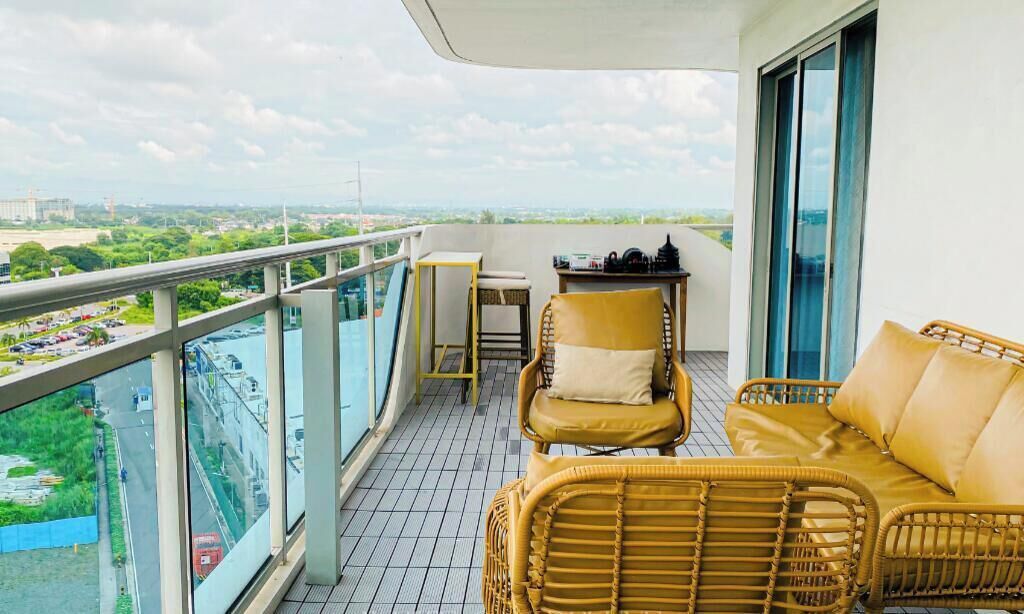 A balcony with wicker furniture, a table, and a view of a cityscape.