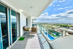 A balcony with a view of a cityscape, a pool, and two wicker chairs. - Family One Bedroom with Manmade Beach View & Mt Arayat View (San Fernando)