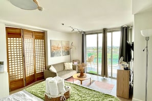 A hotel room with a bed, a sofa, a small table, a lamp, a TV, and a balcony with a view. - Family One Bedroom with Manmade Beach View & Mt Arayat View (San Fernando)
