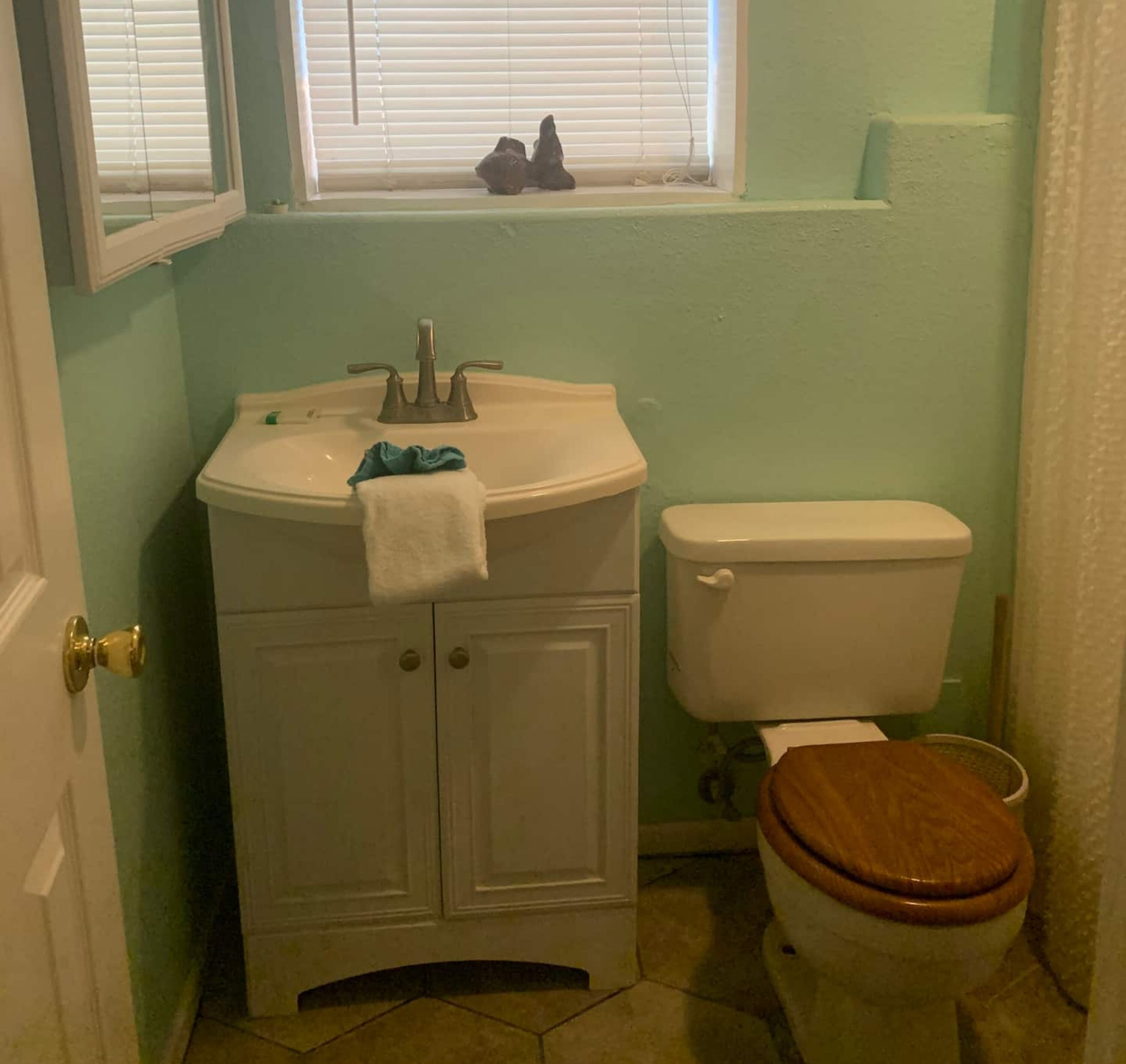 A bathroom with a white sink, a toilet, and a window with blinds.