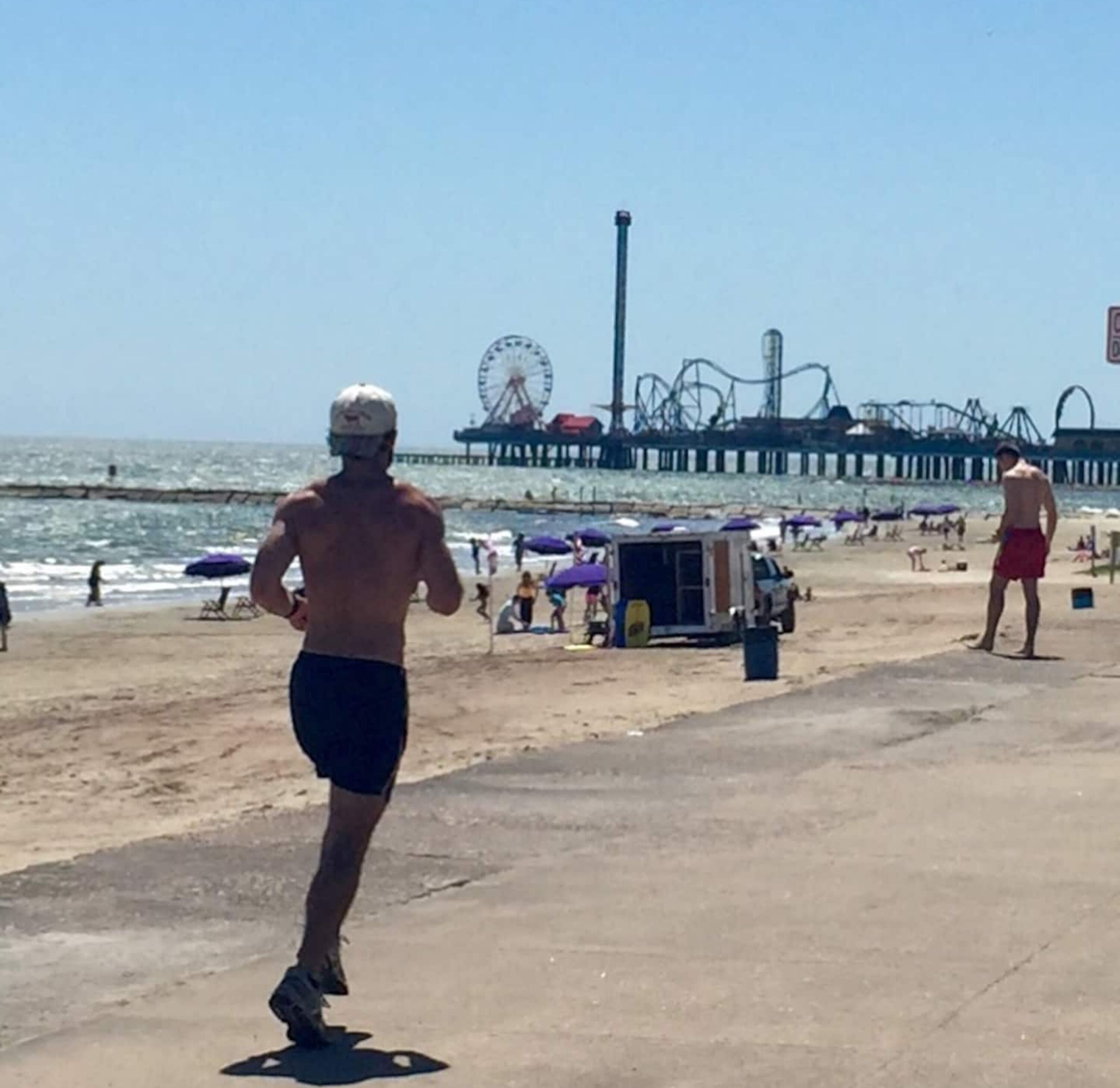 A beach with a pier, a Ferris wheel, and a roller coaster in the background.