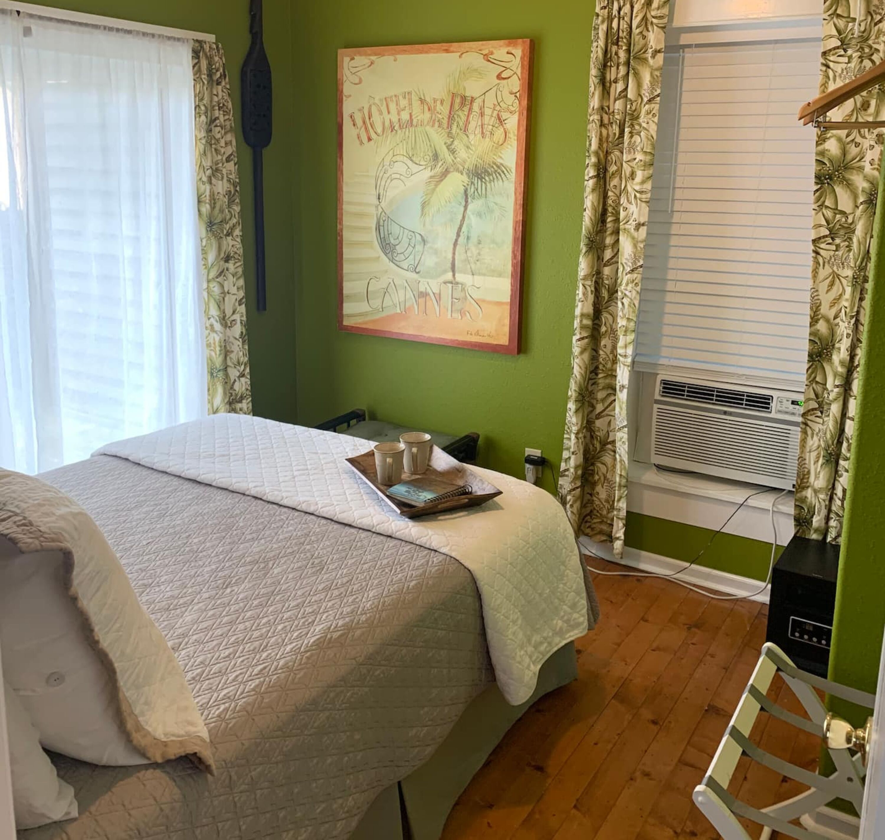A room with a bed, a painting, an air conditioning unit, and a window with curtains.