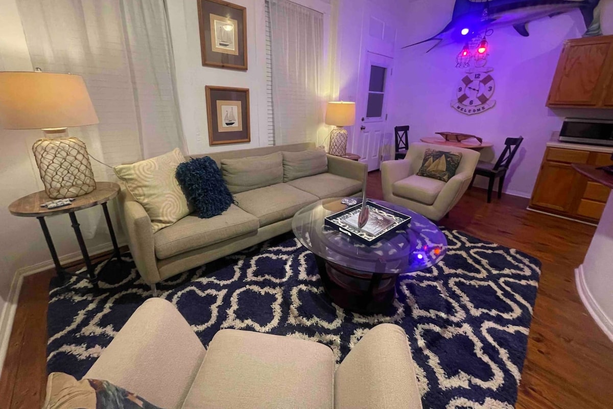 A living room with a sofa, armchairs, a coffee table, a patterned rug, and a wall-mounted clock.