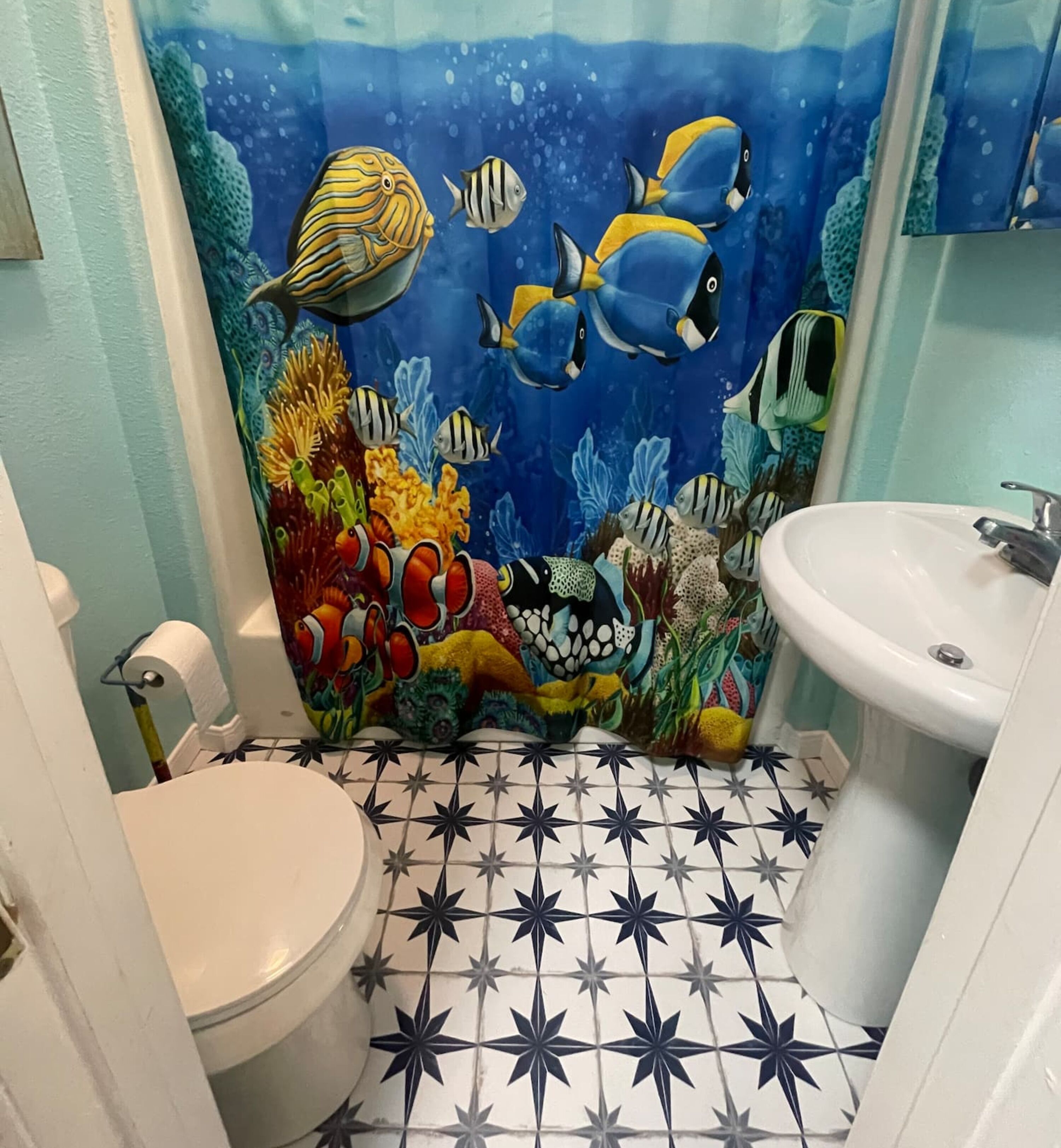 A bathroom with a star-patterned floor, a toilet, a sink, and an underwater-themed shower curtain.