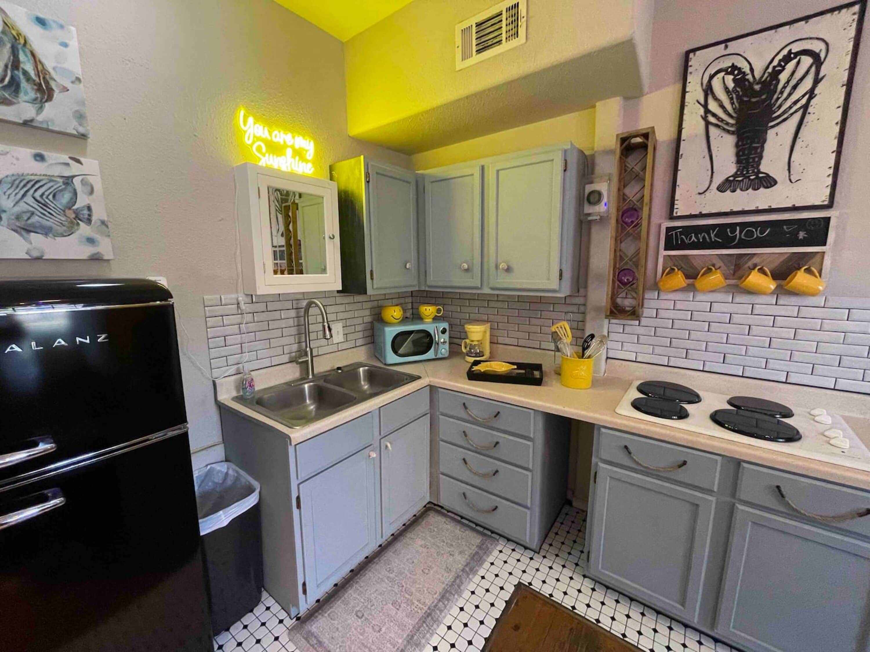 Una cocina con un letrero de neón, un refrigerador, un lavamanos, armarios y un microondas.
