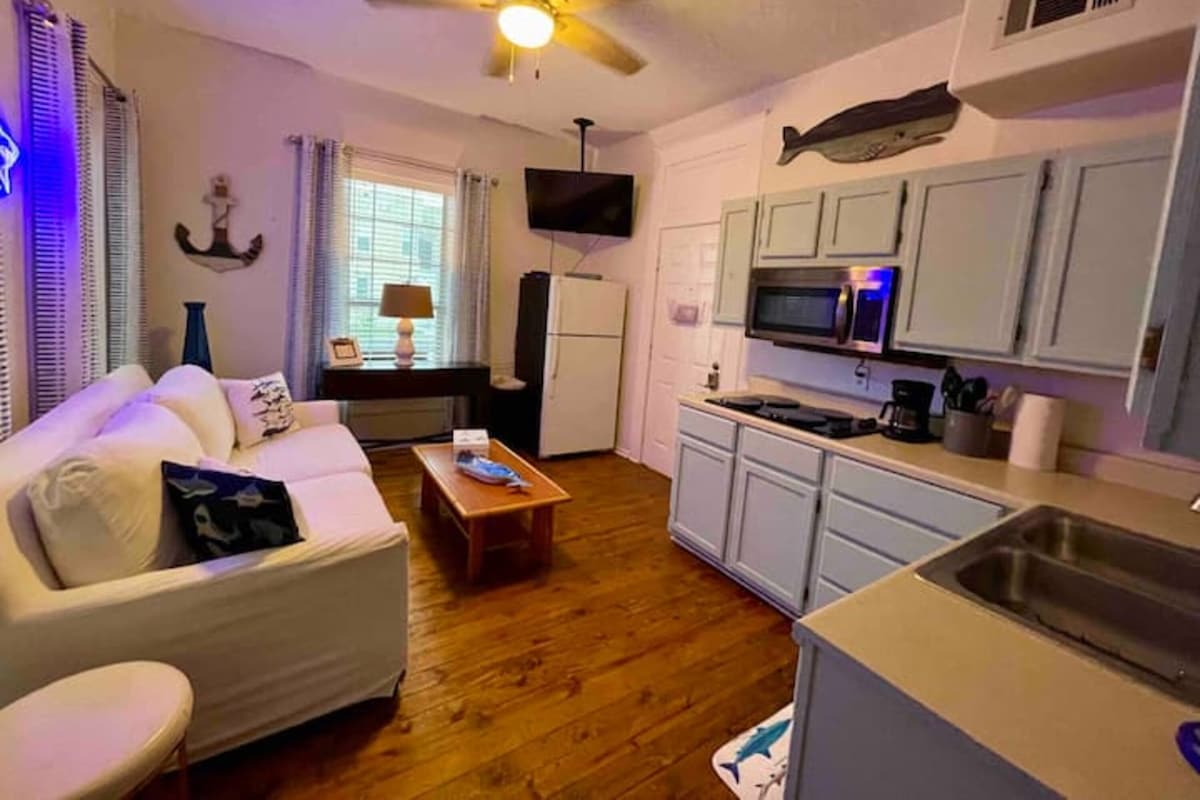 A compact living space with a sofa, coffee table, TV, kitchenette, and a ceiling fan.