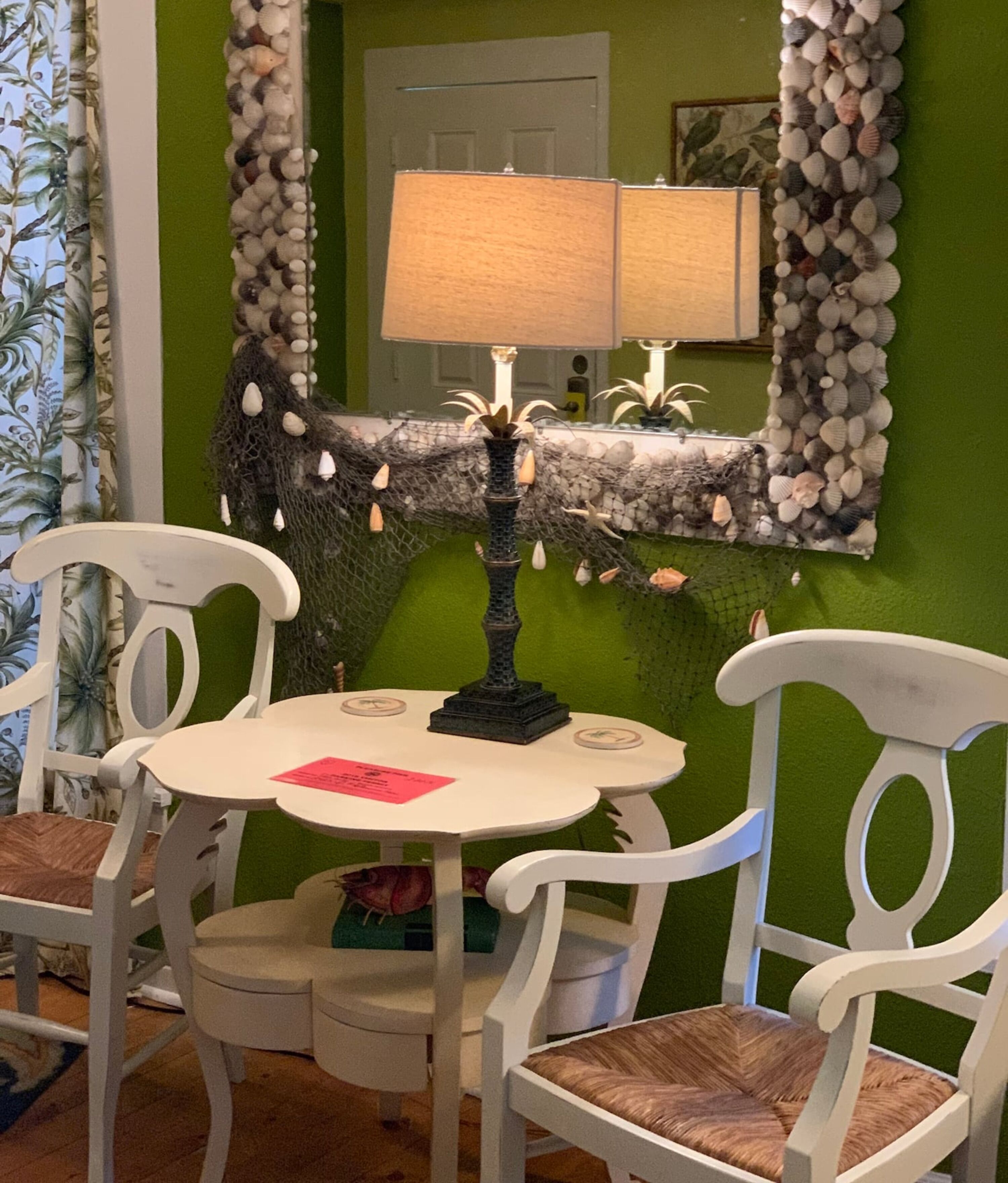 A dining area with a round table, white chairs, a decorative lamp, and a green wall.