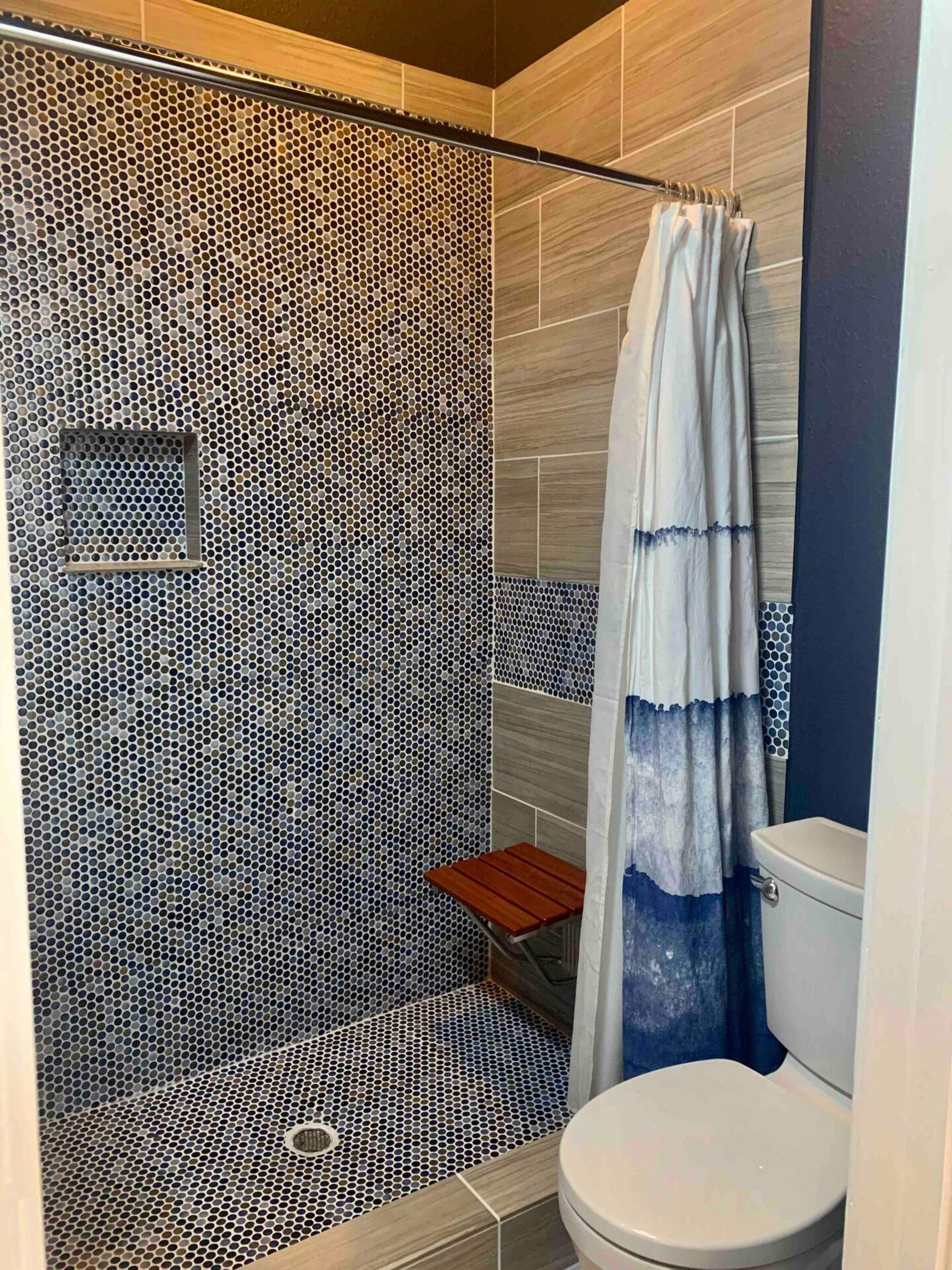 Et badeværelse med bruseområde, karakteriseret ved en væg med huller, en træbænk og et toilet.