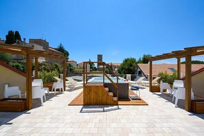 Un terrat amb terrassa, una banyera hidromassatge, pèrgoles de fusta i cadires blanques.
