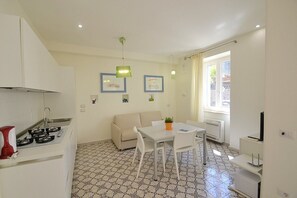 Una cuina compacta amb zona de menjador, un sofà i una finestra amb cortines.